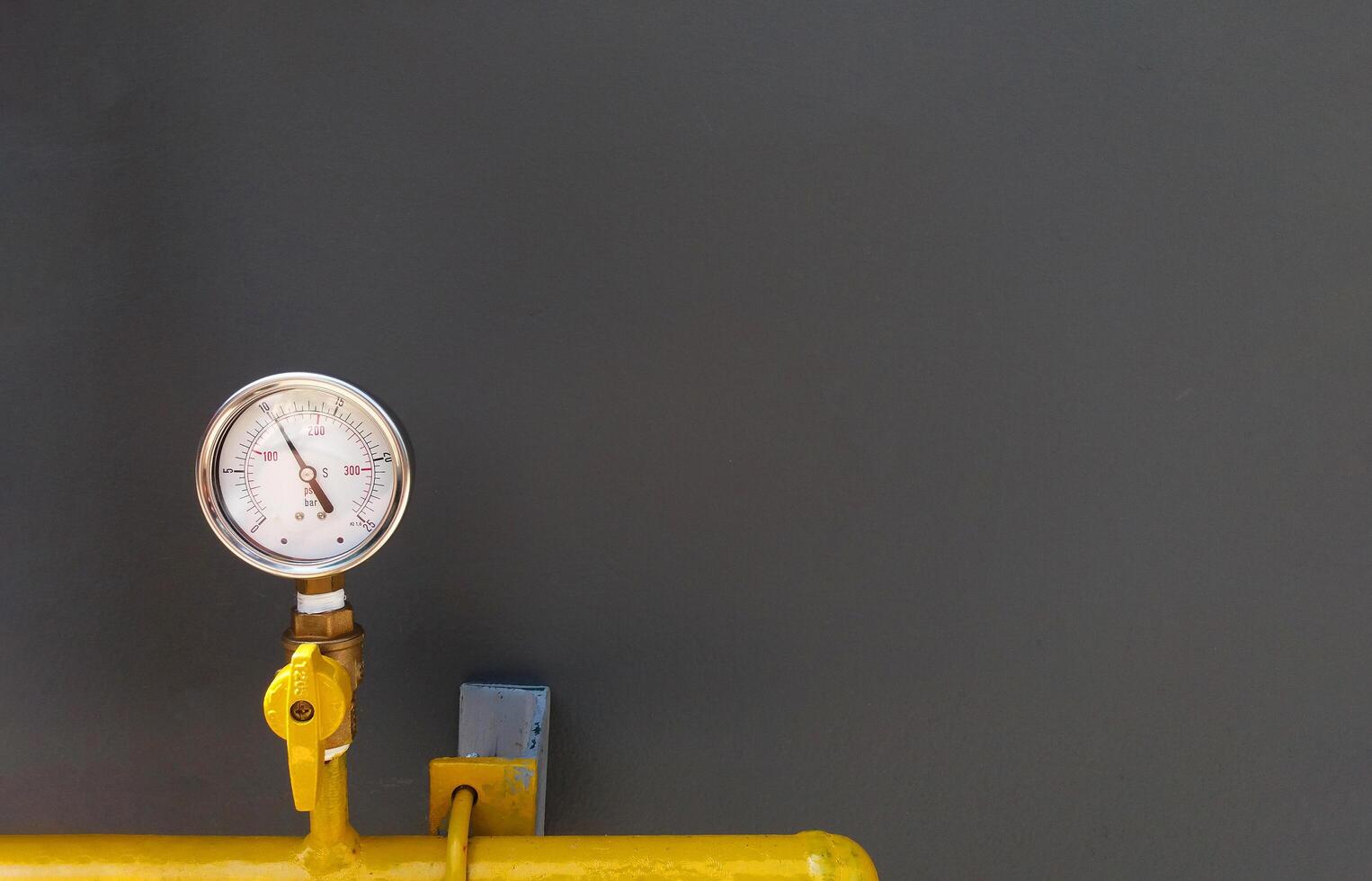 Water, oil or gas pressure gauge with yellow pipe installed on gray wall with copy space. Value gauge with pipeline on grey background. photo