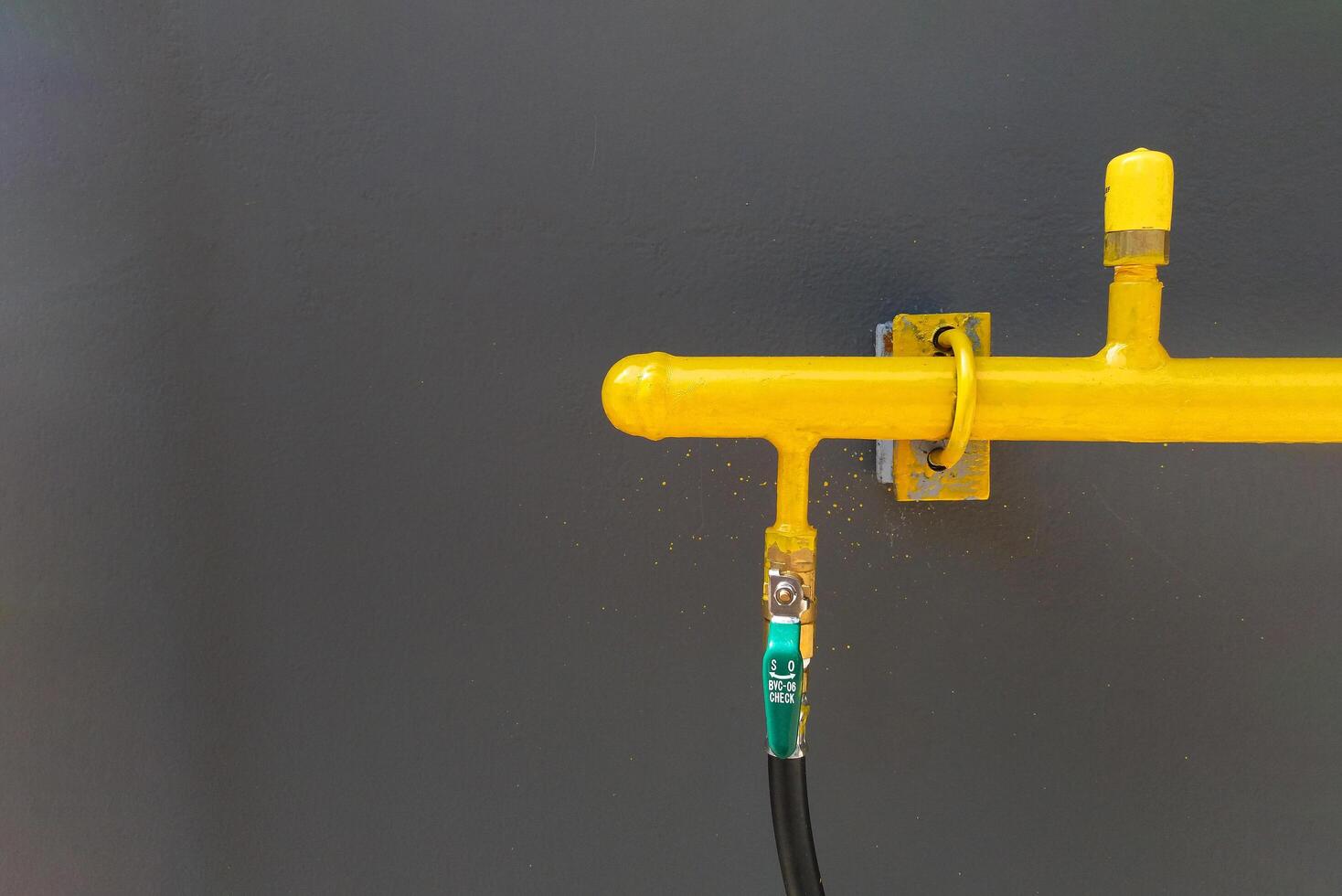 Yellow gas, water or oil pipeline with black cable installed on gray wall with copy space. Pipe on grey background, Industrial and factory concept. photo