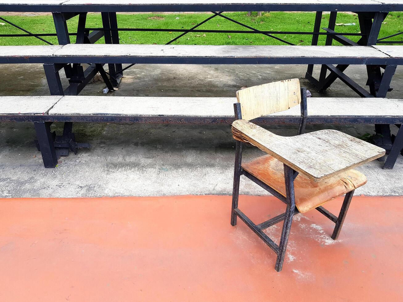 Old school desk putting outdoor in sport field with amphitheater or seat background and left copy space. Damaged object concept. photo