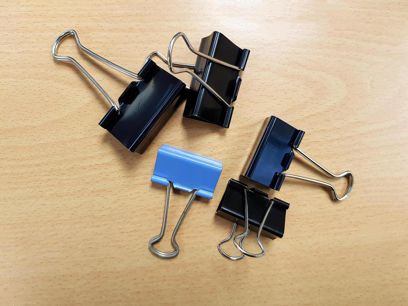 Blue paperclip among black paperclip on light brown wooden table. Group of object, Office or Education accessory and Differential, Social divide or Conflict and Encircle concept. photo