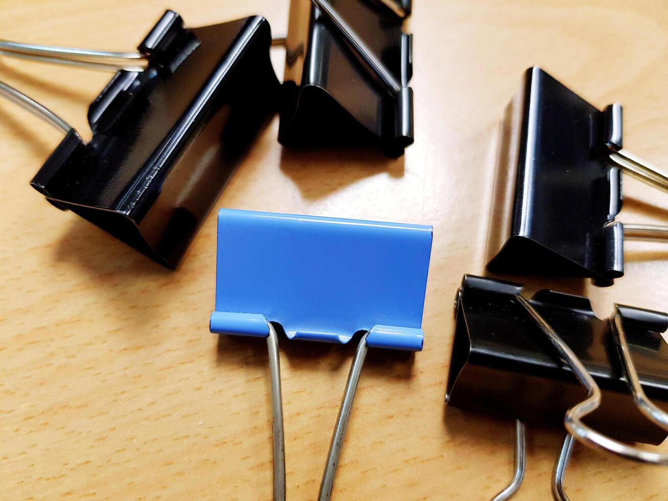 Close up Blue paperclip putting among black paperclip on light brown wooden table. Group of object, Office or Education accessory and Differential, Social divide or Conflict and Encircle concept. photo