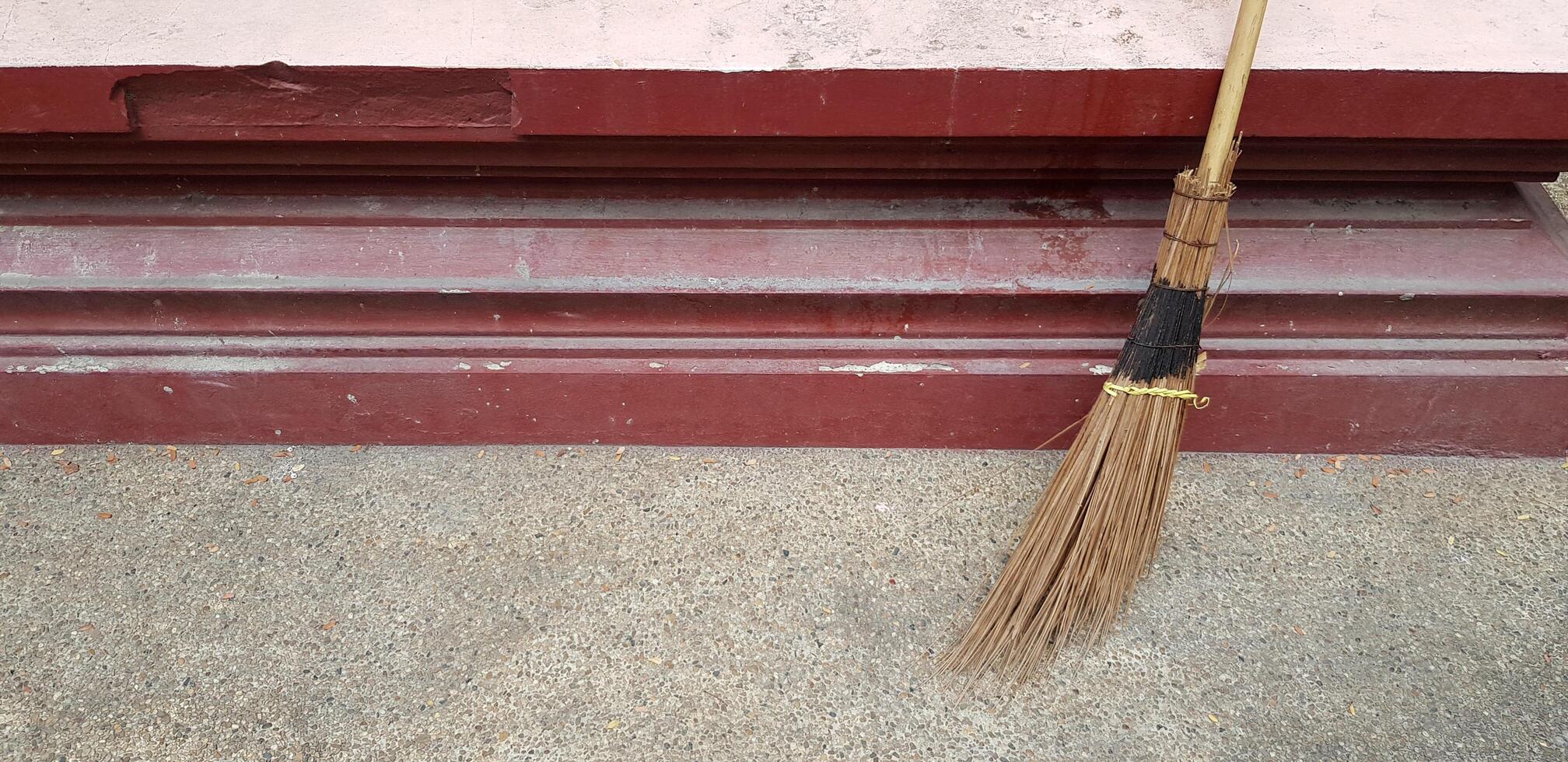 Broom Against the red wall for clean dust and sweep the garbage with left copy space. Cleaning tool and Housework concept. photo