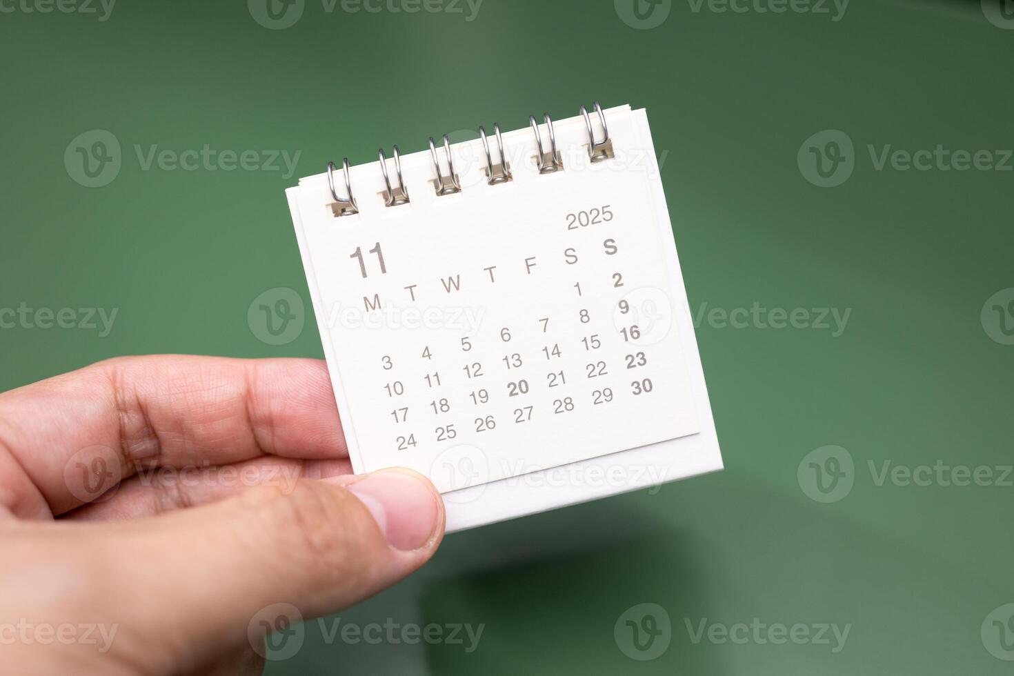 Hand holding mini calendar for NOVEMBER 2025 background. Calendar concept with 2025 NOV calendar. Calendar on green background. photo