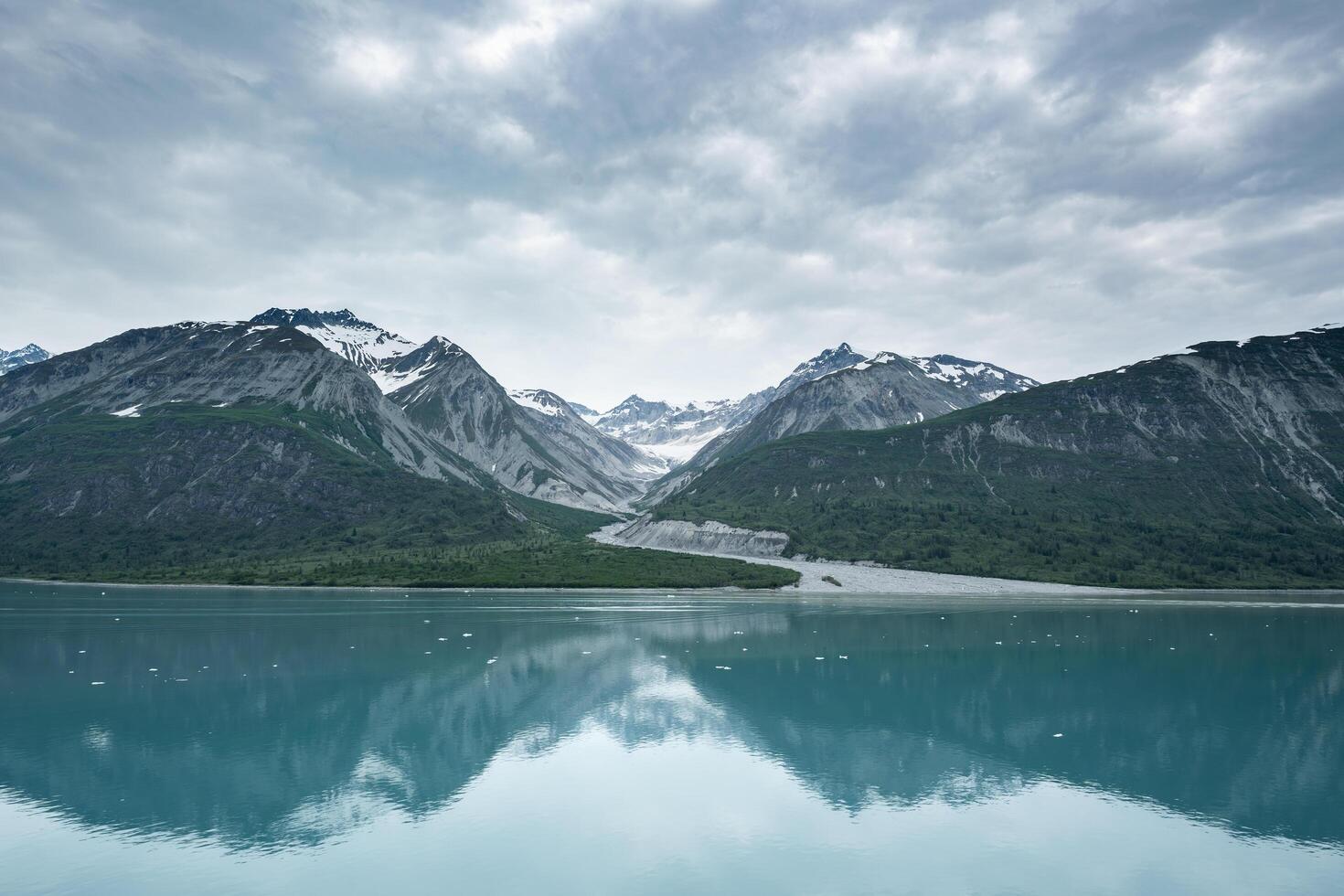 Beautiful snowy mountain peaks rising up from the shoreline of a calm body of water with a stunning reflection below and a cloudy sky overhead. photo
