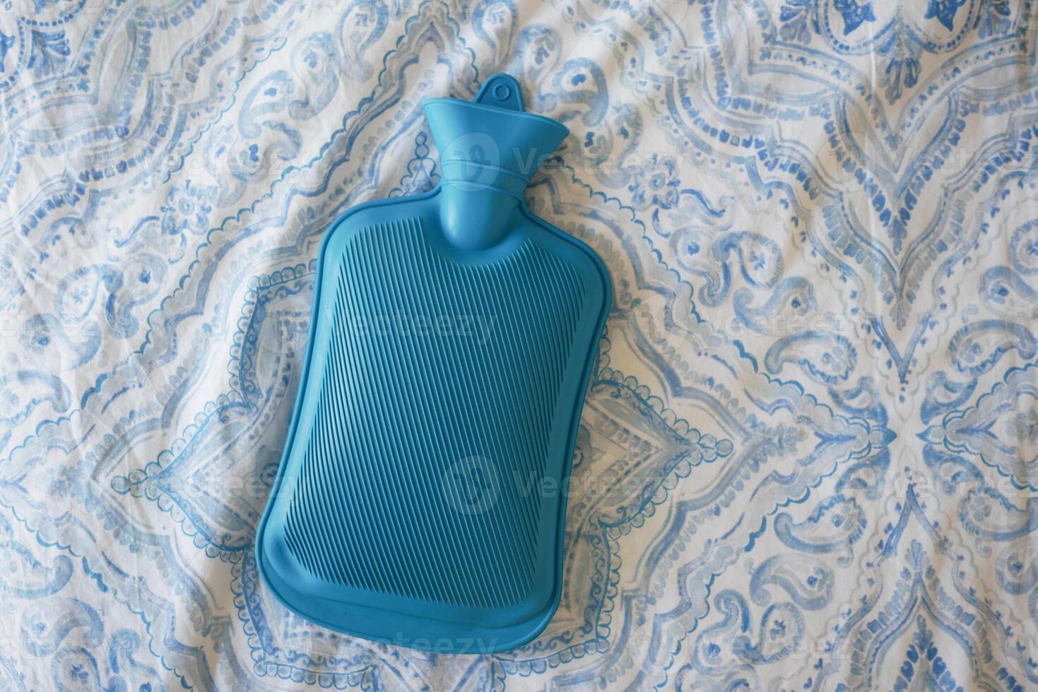 A Blue Hot Water Bottle resting comfortably on a Soft Patterned Blanket photo
