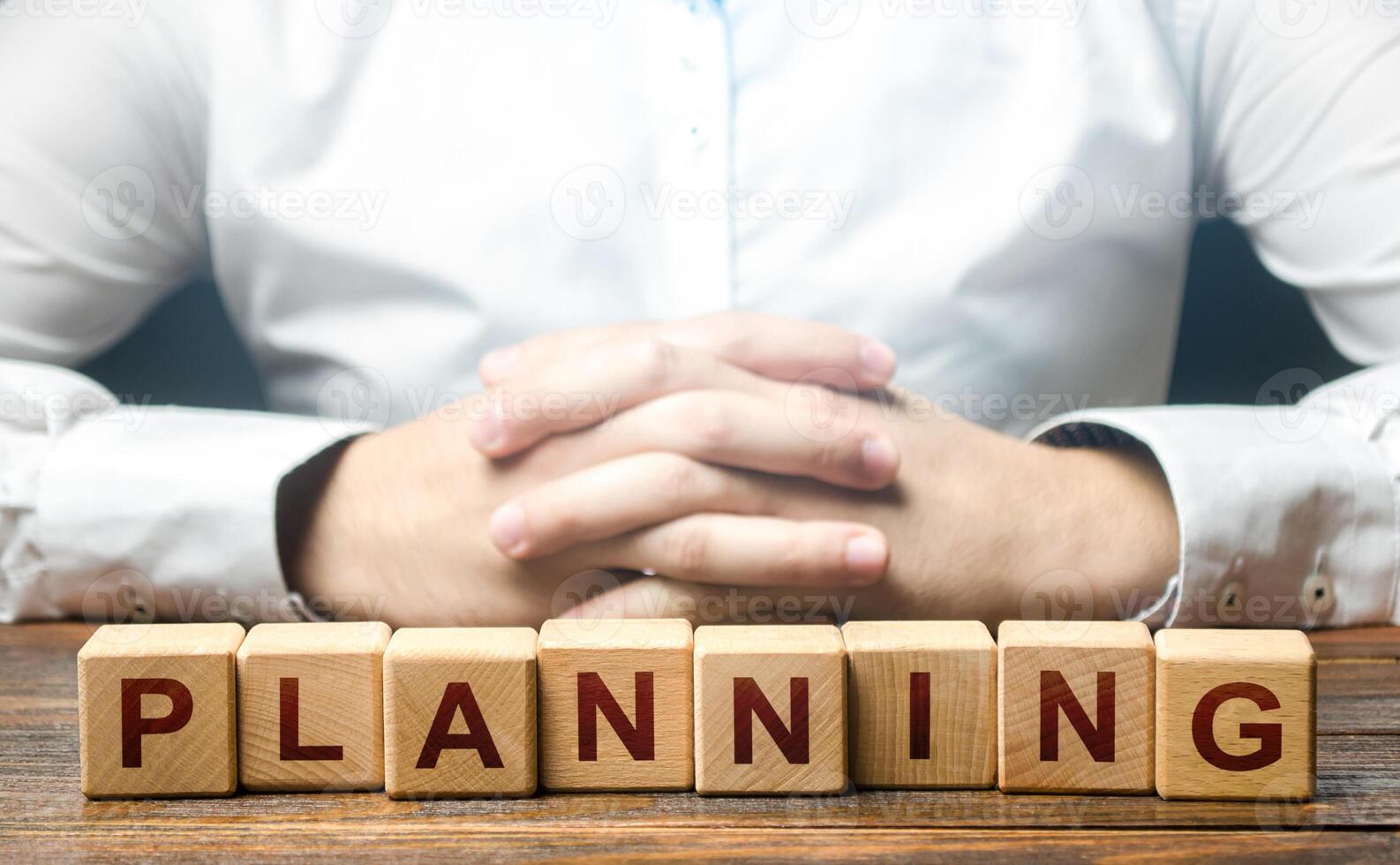 Man folded his hands on a background of blocks with the word Planning. Leadership quality to plan the best options for further action. Provide for any possible consequences. Discretion, determination photo