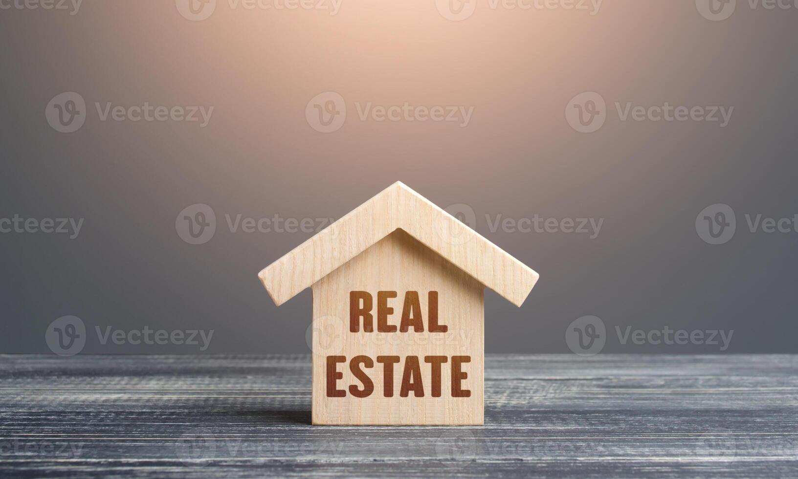 Wooden figurine of a house with word Real Estate. Buying and selling. Housing, realtor services. Construction industry, building maintenance. Mortgage loan. Assets and tax payments. Stamp duty photo