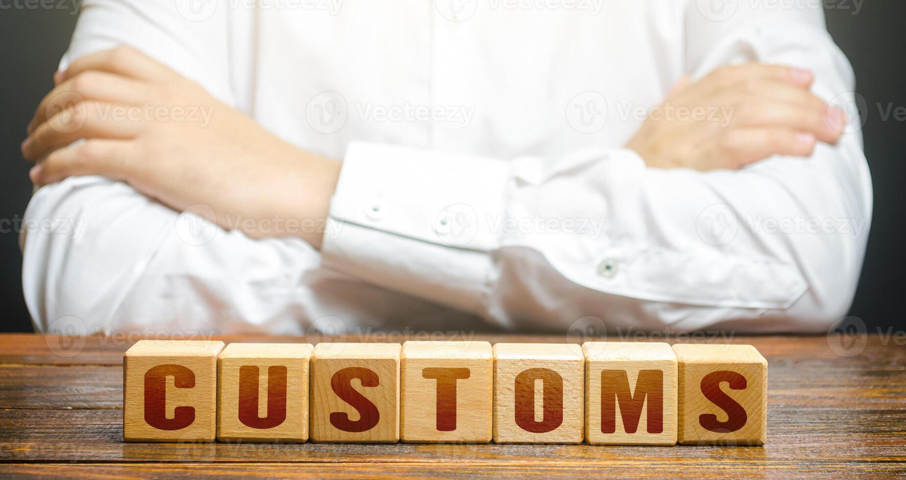 Man with folded hands on his torso and blocks with word Customs. Customs border control. Tariffs and taxes on the import of goods and products. Imports monitoring. Duties. Transportation and transit. photo