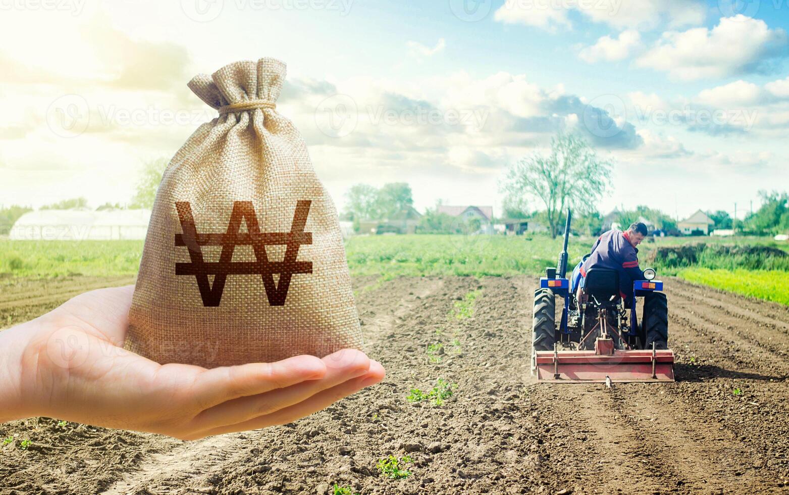 Hand with south korean won and a farmer on a tractor works on farm field. Financial support, subsidies for agriculture. Farm loans, economic preferences. Purchase or lease rent of land. photo