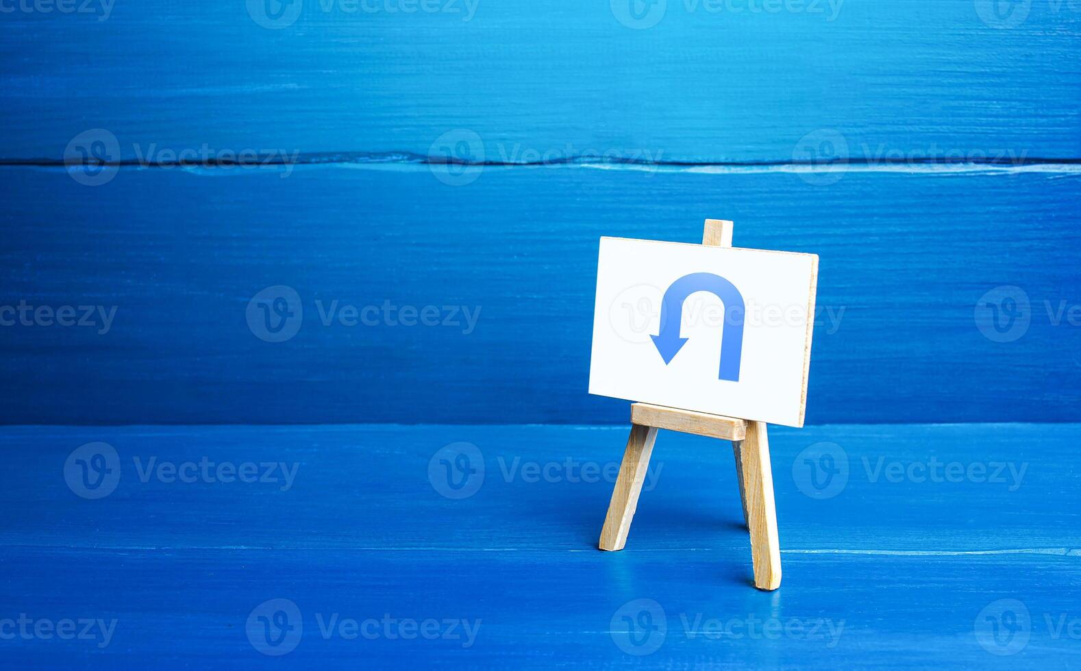 Easel with arrow turning back. Change plans, circumstances. Tactical retreat. Avoiding problems, reducing risks. Reassessment of actions. Break a promise. Find other way. Return to source. Step back. photo