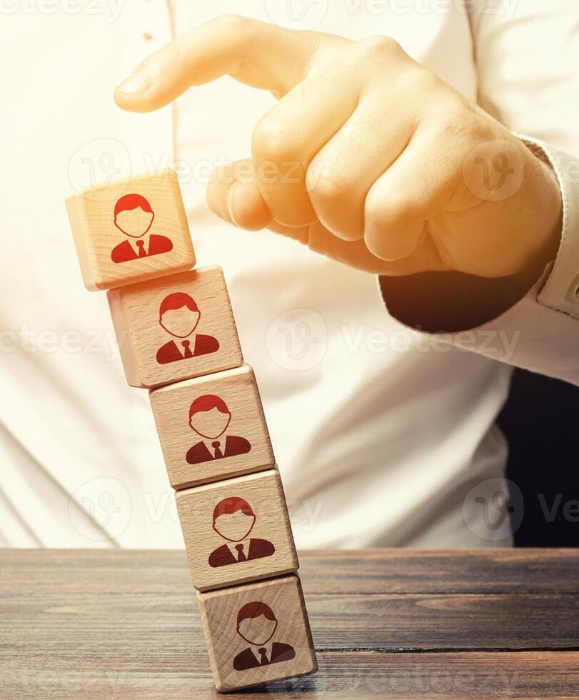 Man knocks down a tower of blocks with employees. Mass layoffs, closing a business company. Dismissal workers. Poor leadership. Disbandment of team collective. Elimination of competitors, repression. photo
