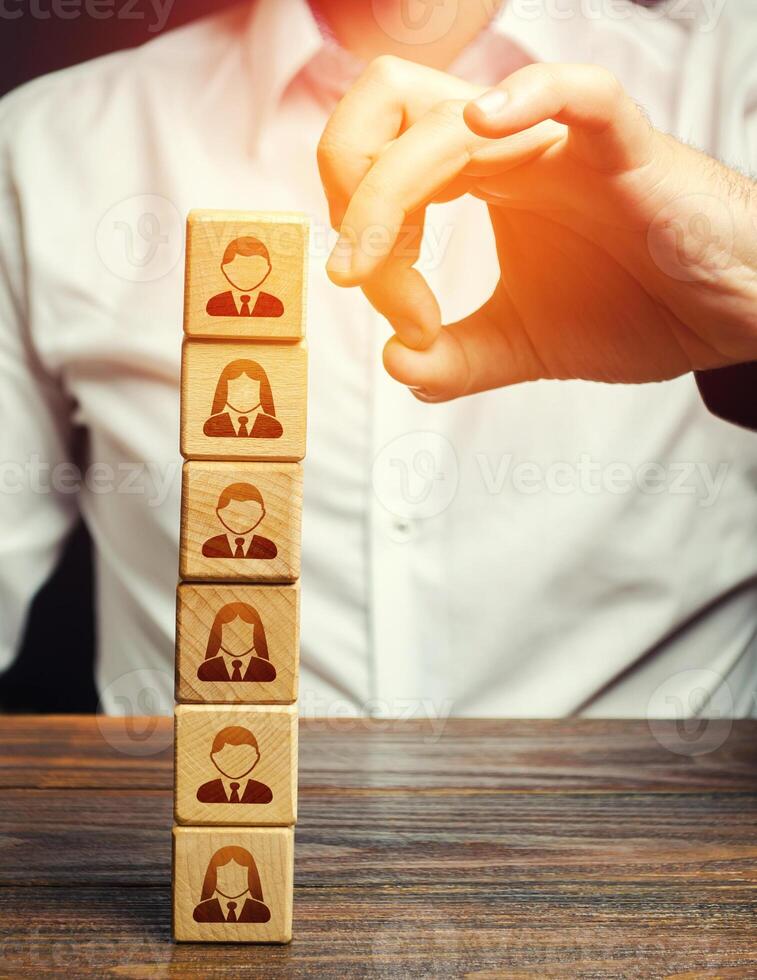 Man knocks down a tower of blocks with employees. Mass layoffs, closing a business company. Dismissal workers. Elimination of competitors, repression. Poor leadership. Disbandment of team collective. photo