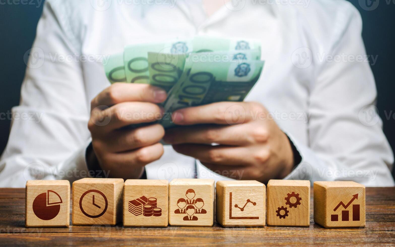 A man is counting money and blocks with business attributes. Good business model. Profitability. The rules for successful investment. High performance, great work. Company management photo
