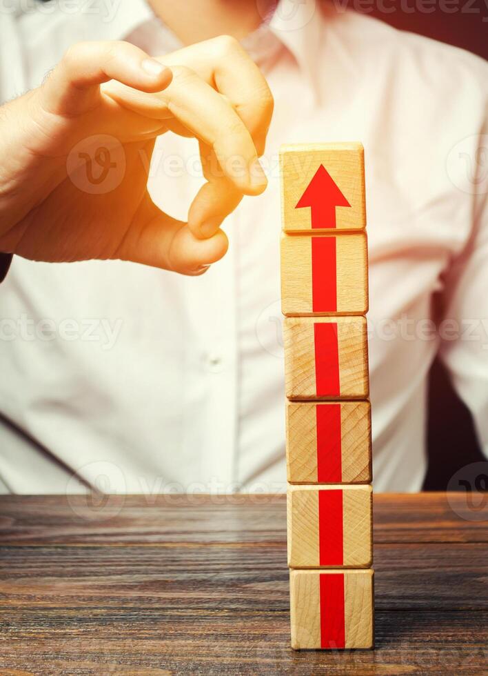 A man knocks down a tower of blocks with an arrow up. End of career, stop the progress and achievements. Eliminate the phenomenon, prevent further growth. Disruption business processes. Sabotage. photo
