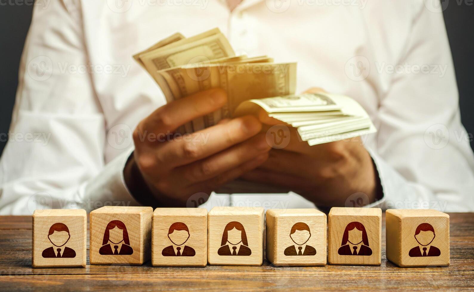 A man is counting money in his hands over blocks with symbols of employees. Wage fund. Accounting and budgeting. Payday. Expanding a profitable business, recruiting and training employees. photo