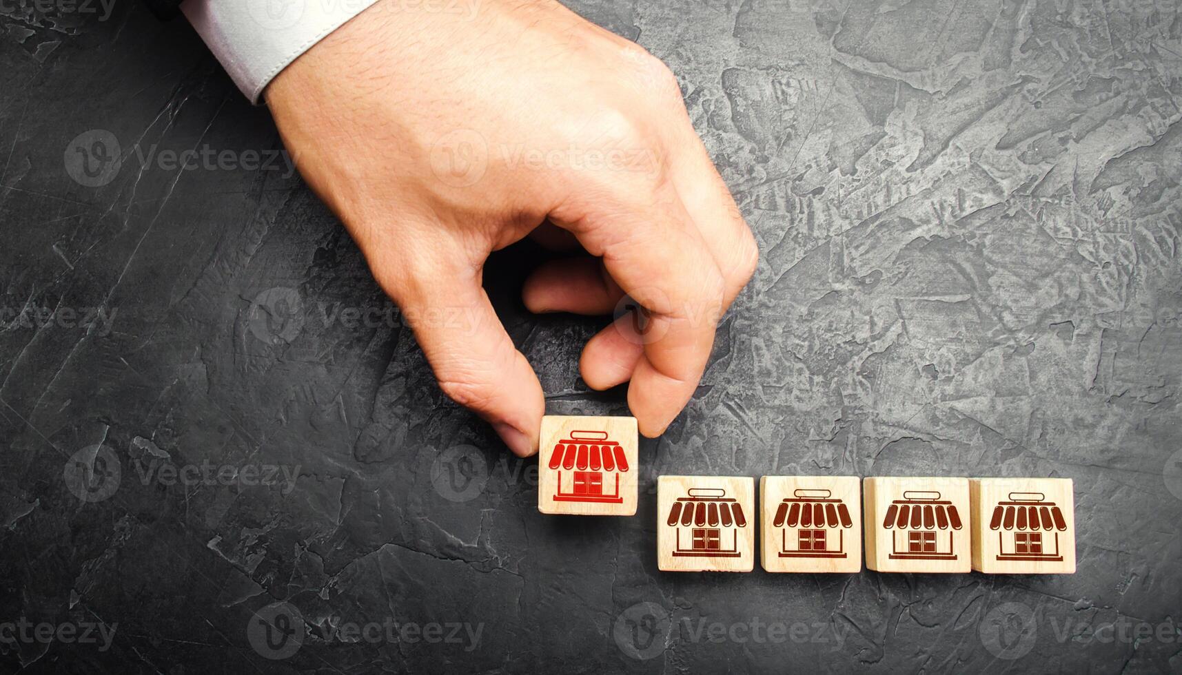 Man Adding a block with a store icon to others. Franchise commercial concession concept. Investing in asuccessful business model. Building a business empire. Expansion and competitive growth photo