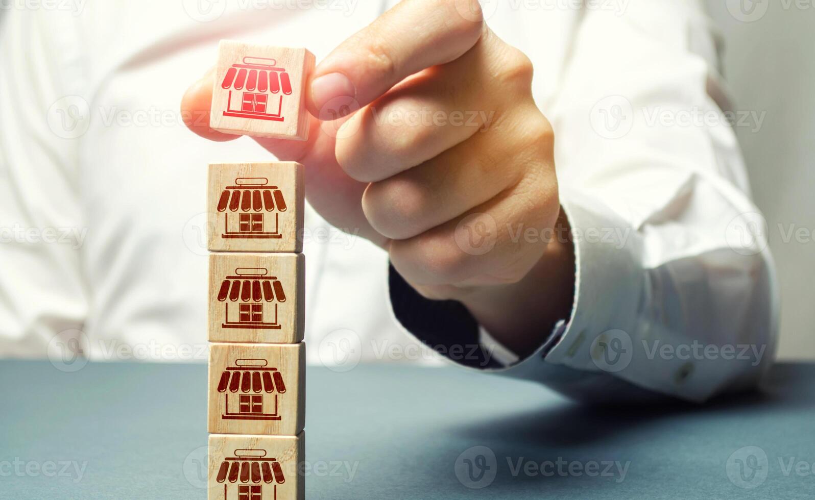 Female hand builds a tower of blocks with store icons. Building a business empire. Franchise commercial concession concept. Investing in asuccessful business model. Expansion and competitive growth photo