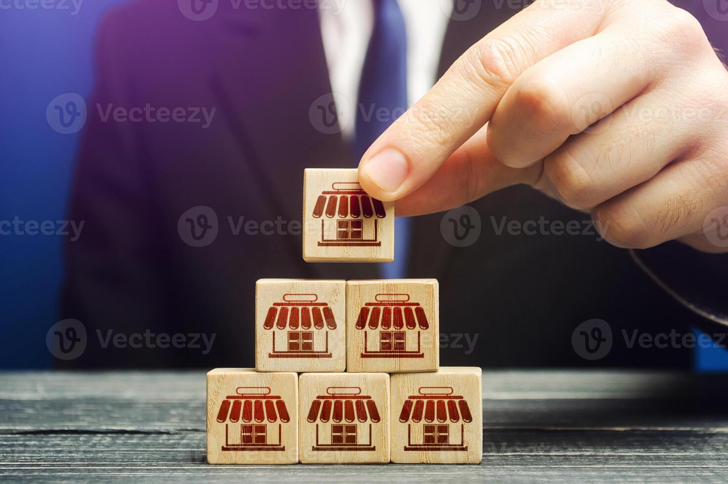 A man builds a pyramid from blocks of business shops. Building a successful business empire. Expansion and competitive growth. Franchise concession concept. Commercial network development. photo