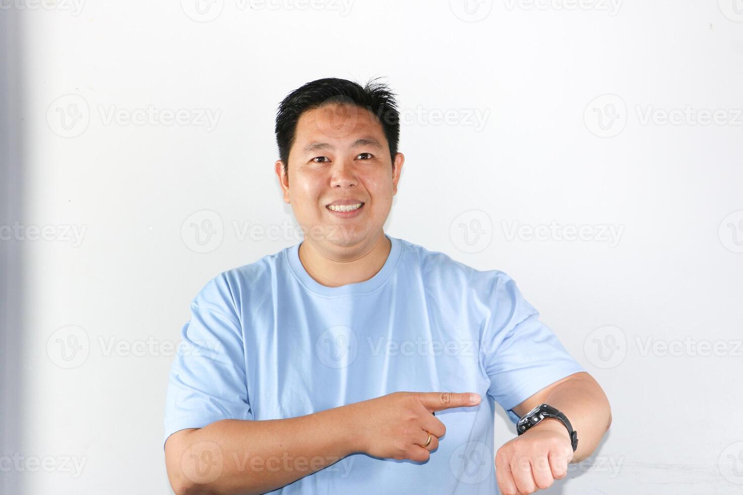 Happy face expression and smiling gesture of Asian man pointing his finger to his watch for being on time in important appointment or meeting. photo