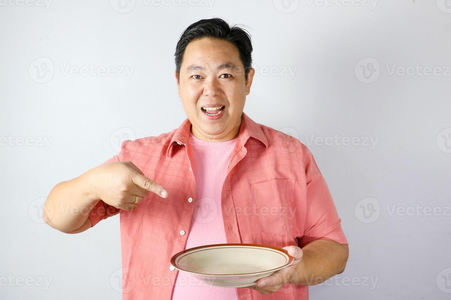 A man wearing pink shirt with smiling happy face and pointing his finger to brown empty dining plate. photo