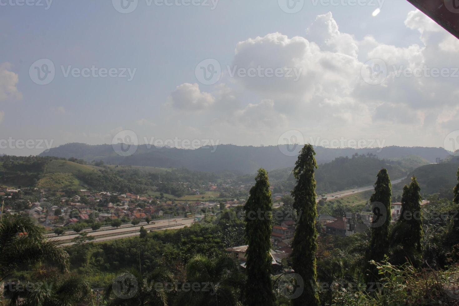 Hills and a highway with green trees and clear skies offering a view of a town on a sunny day photo