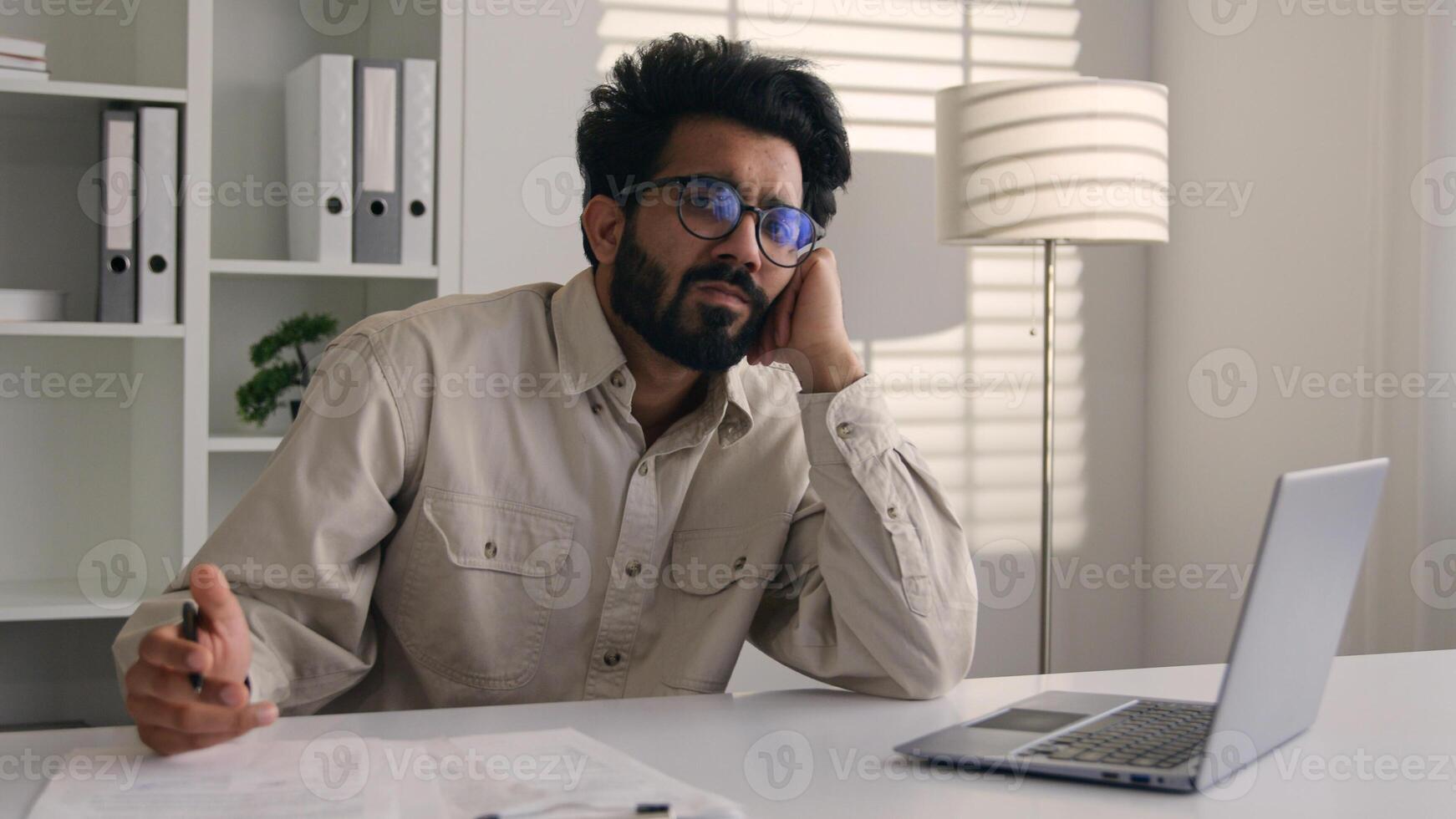 Tired exhausted weary Arabian Indian businessman bored employee designer sad sleepy unproductive at modern office work with laptop computer project boring burnout apathy business man lazy write notes photo