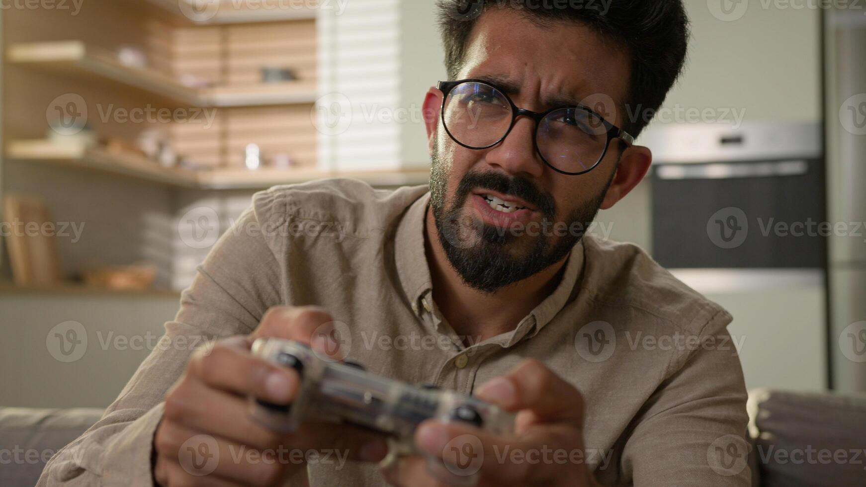 Indian Arabian man ethnic guy have fun on sofa couch play online game smart TV console virtual driving car use wireless controller entertainment in home kitchen male gamer playing with joystick photo