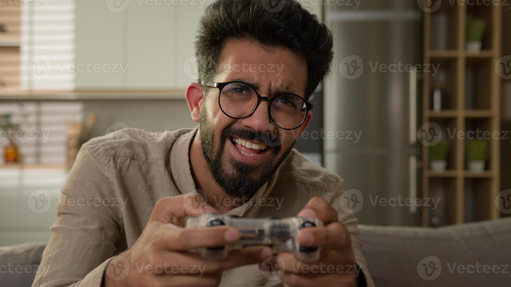 Addicted male gamer Arabian Indian man guy on couch play game using remote controller joystick virtual reality gaming addiction playing console cyber match on TV home entertainment in kitchen photo