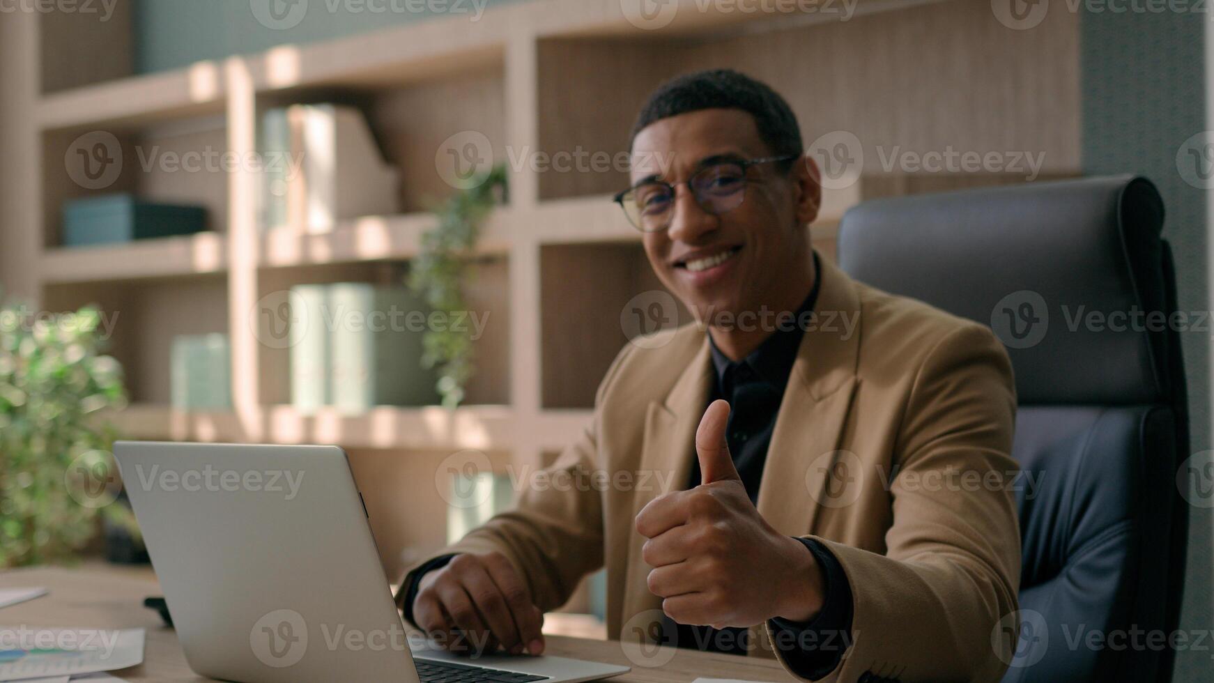 African American 30s millennial business man happy businessman smiling entrepreneur office manager working laptop typing on computer looking camera smile show thumb up gesture aprove recommend like photo