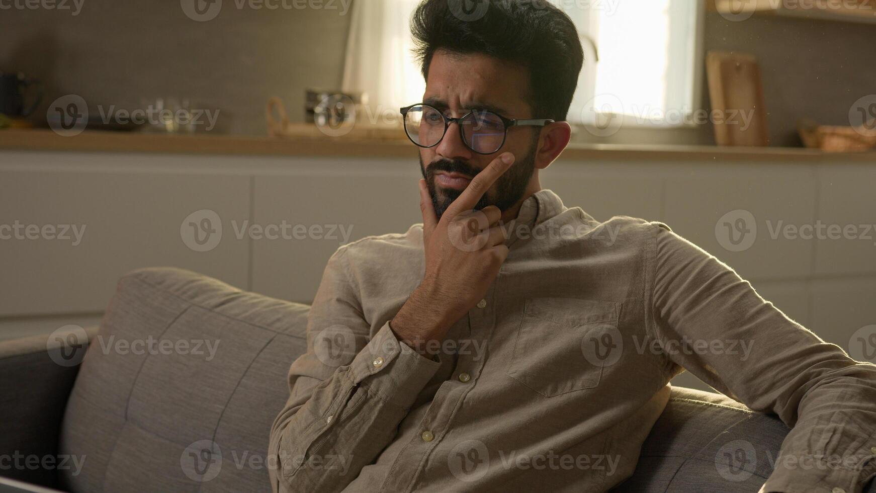 Pensive thoughtful Indian Arabian ethnic man puzzled guy at home apartment kitchen think difficult decision solve issue unhappy male rest alone on couch thinking deep thoughts consider doubt question photo
