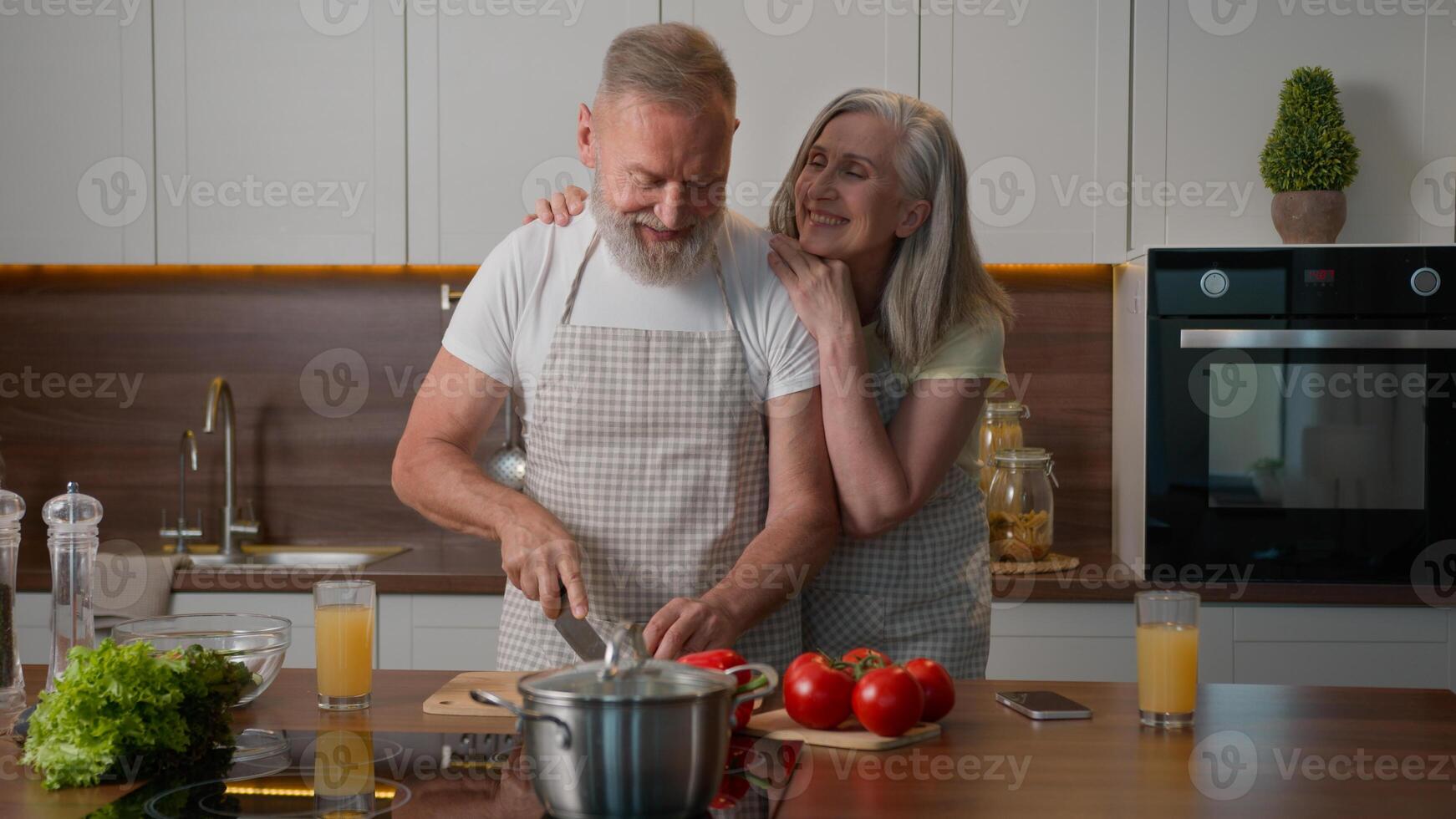 Caucasian happy old family retired middle aged mature couple woman and man love cooking together at home kitchen cut fresh vegetables healthy food caring wife hug adorable husband cuddling cook salad photo