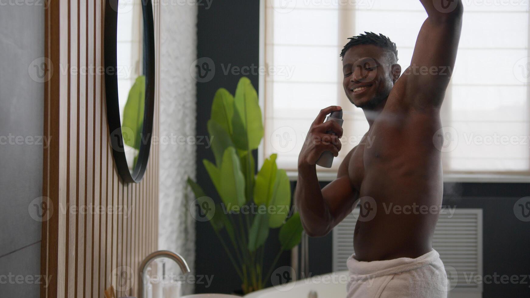 Smiling shirtless African American man applying deodorant antiperspirant in armpit get ready looking in bathroom mirror male everyday hygiene hyperhidrosis treatment sweat protection daily skincare photo