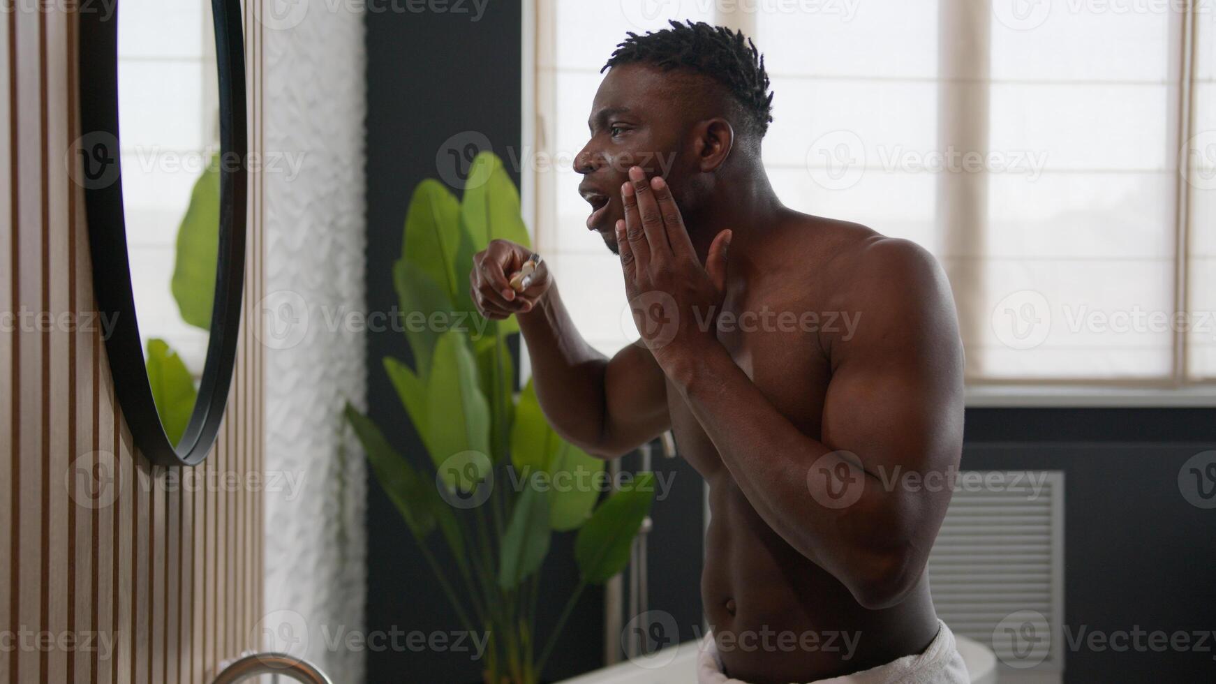 African American man brushing teeth with toothbrush feeling toothache pain hurt sensitive bleeding gums periodontitis inflammation tooth decay oral cavity caries problem hygiene procedure in bathroom photo
