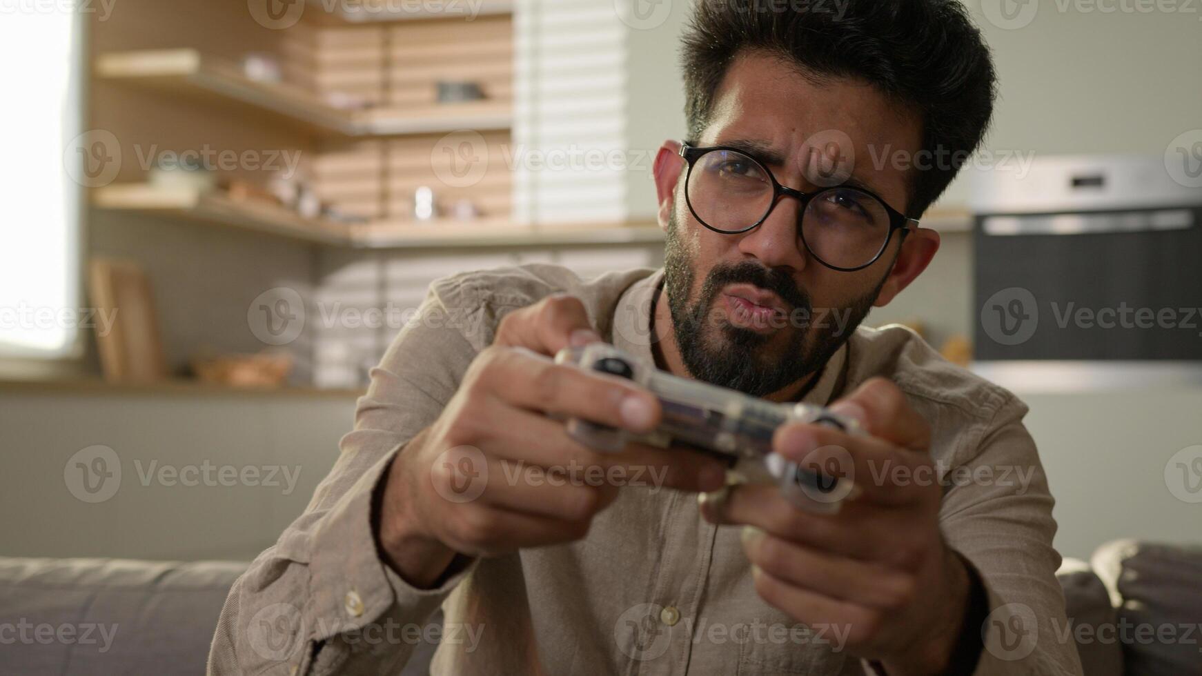 Addicted male gamer Arabian Indian man guy on couch play game using remote controller joystick virtual reality gaming addiction playing console cyber match on TV home entertainment in kitchen photo