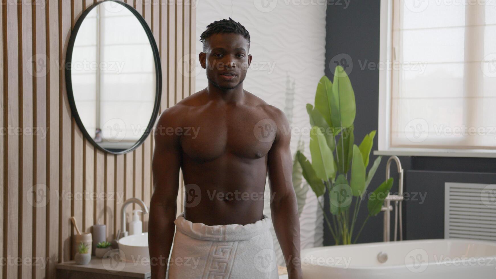 African American man happy muscular hipster smiling in bathroom sexy 30s model with bath towel on hips naked torso showing muscles biceps strong pose raising arms power body care sport health hygiene photo