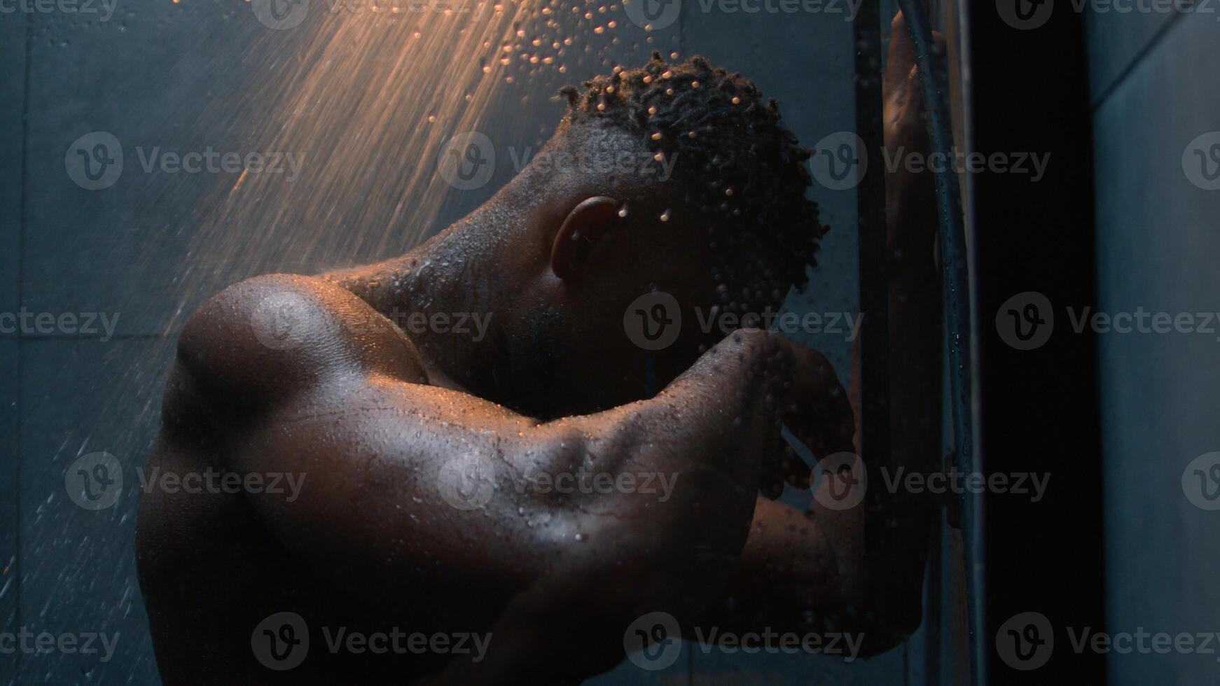 African American muscular strong guy naked wet male sad frustrated man take shower under falling water washing body routine in bathroom suffer depression stress impotence mental psychological tension photo