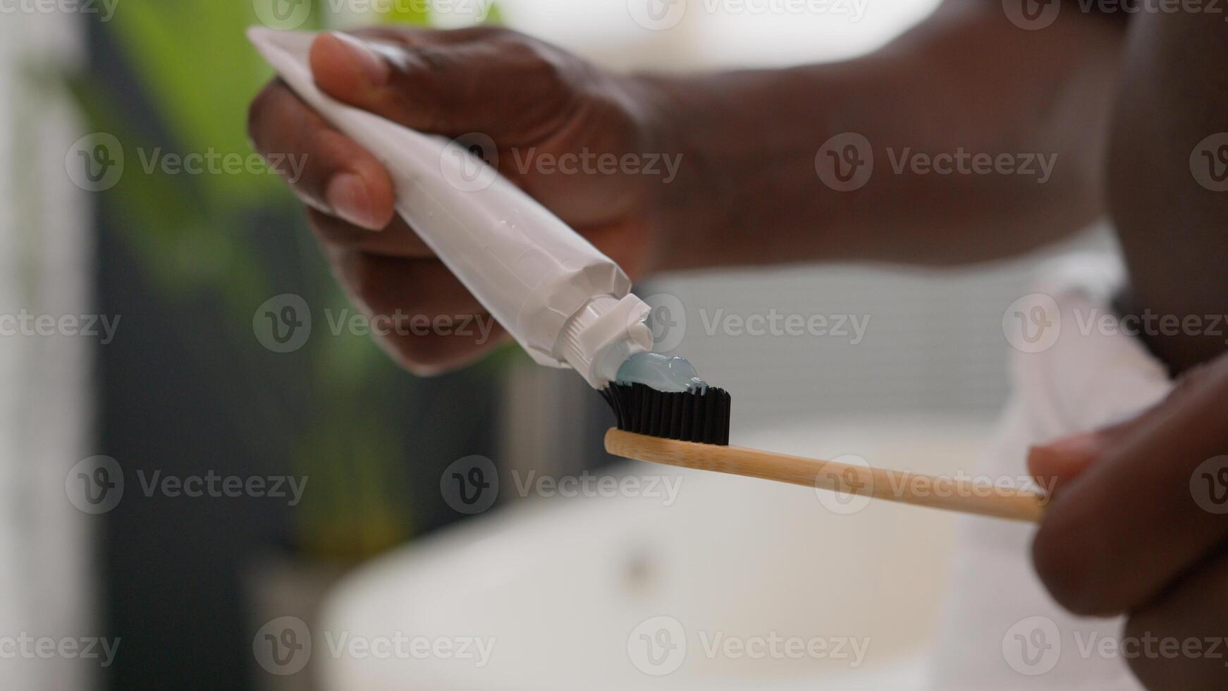 Close up hands squeezing out white toothpaste from tube on toothbrush dental care morning procedure oral hygiene prevent tooth caries unknown African American man prepare brushing teeth in bathroom photo