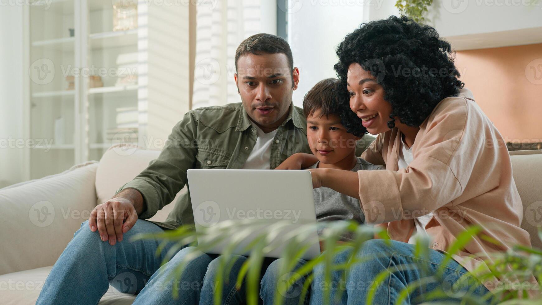 Home interior multiracial family parents child using laptop device together African American mother father and Caucasian little kid boy son winnning prize online lottery victory rejoice in apartment photo
