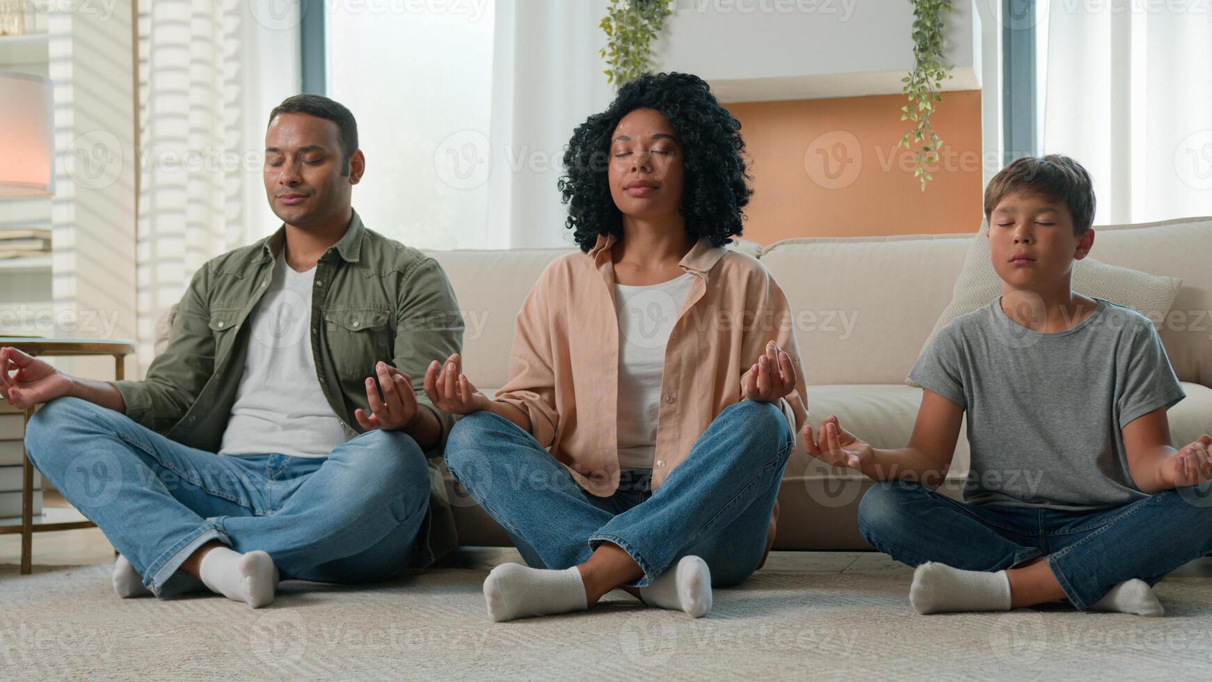 Calm family multiracial African American mother and father meditate with kid boy child yoga exercise in lotus pose on home floor together parents teaching little son zen balance breathing meditation photo