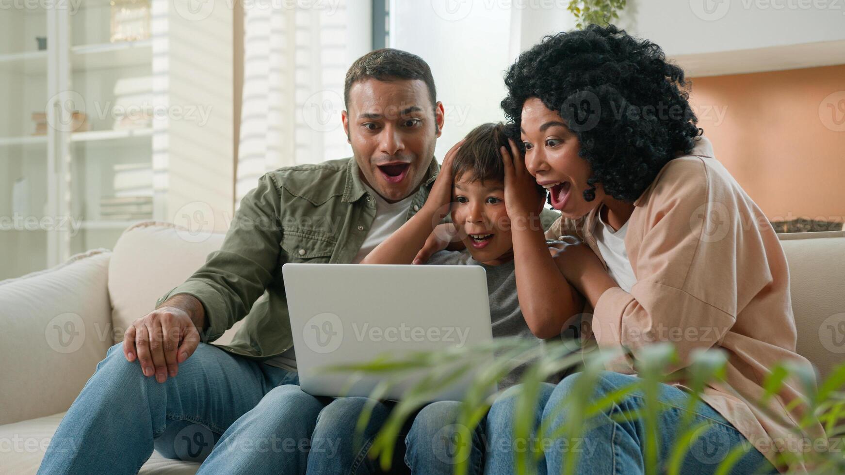 Home interior multiracial family parents child using laptop device together African American mother father and Caucasian little kid boy son winnning prize online lottery victory rejoice in apartment photo
