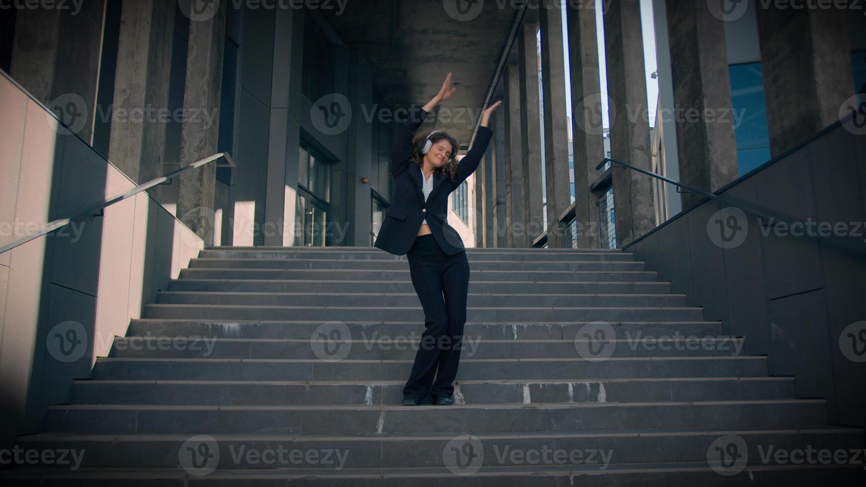 Dancing joyful happy funny Caucasian girl businesswoman listen music headphones enjoy song walking down stairs outside office building pleased professional business woman dance city freedom lifestyle photo