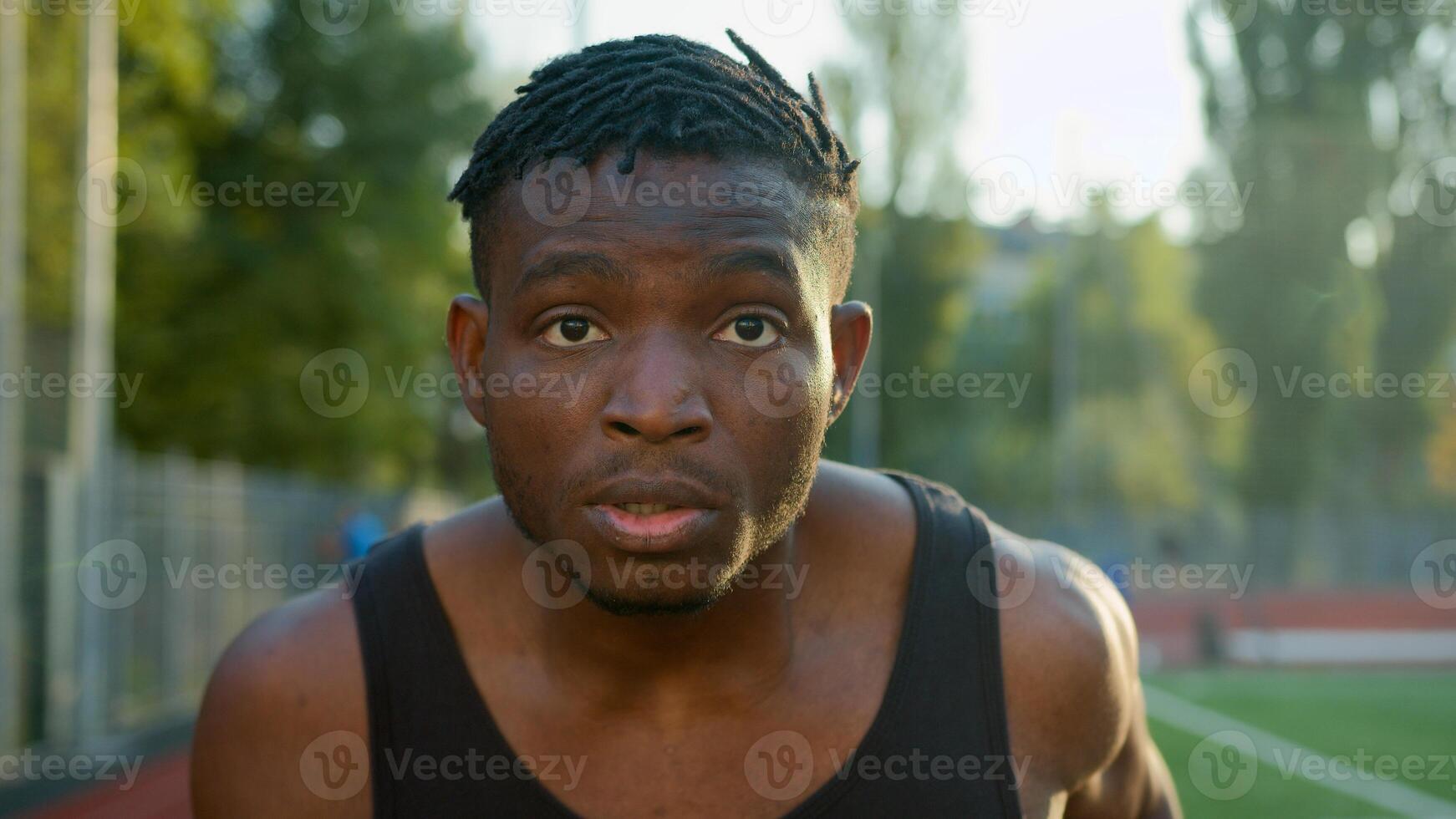 African American ethnic man guy runner jogger sprinter running on race track outdoor stadium sport ground determined male jogging morning workout run jog exercise outside city fast motion motivation photo
