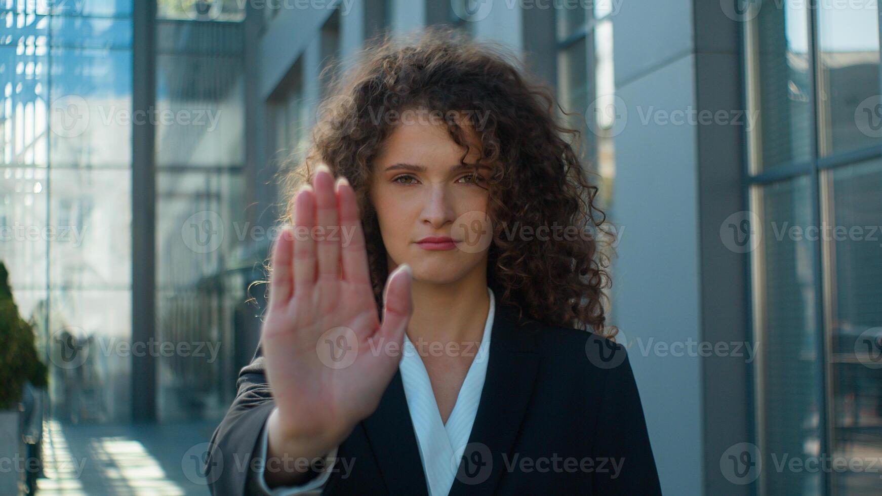 Serious Caucasian business woman businesswoman girl looking at camera showing stop gesture outstretched hand refuse keep distance no not sign prohibit in city outdoors protest protect feminism rights photo