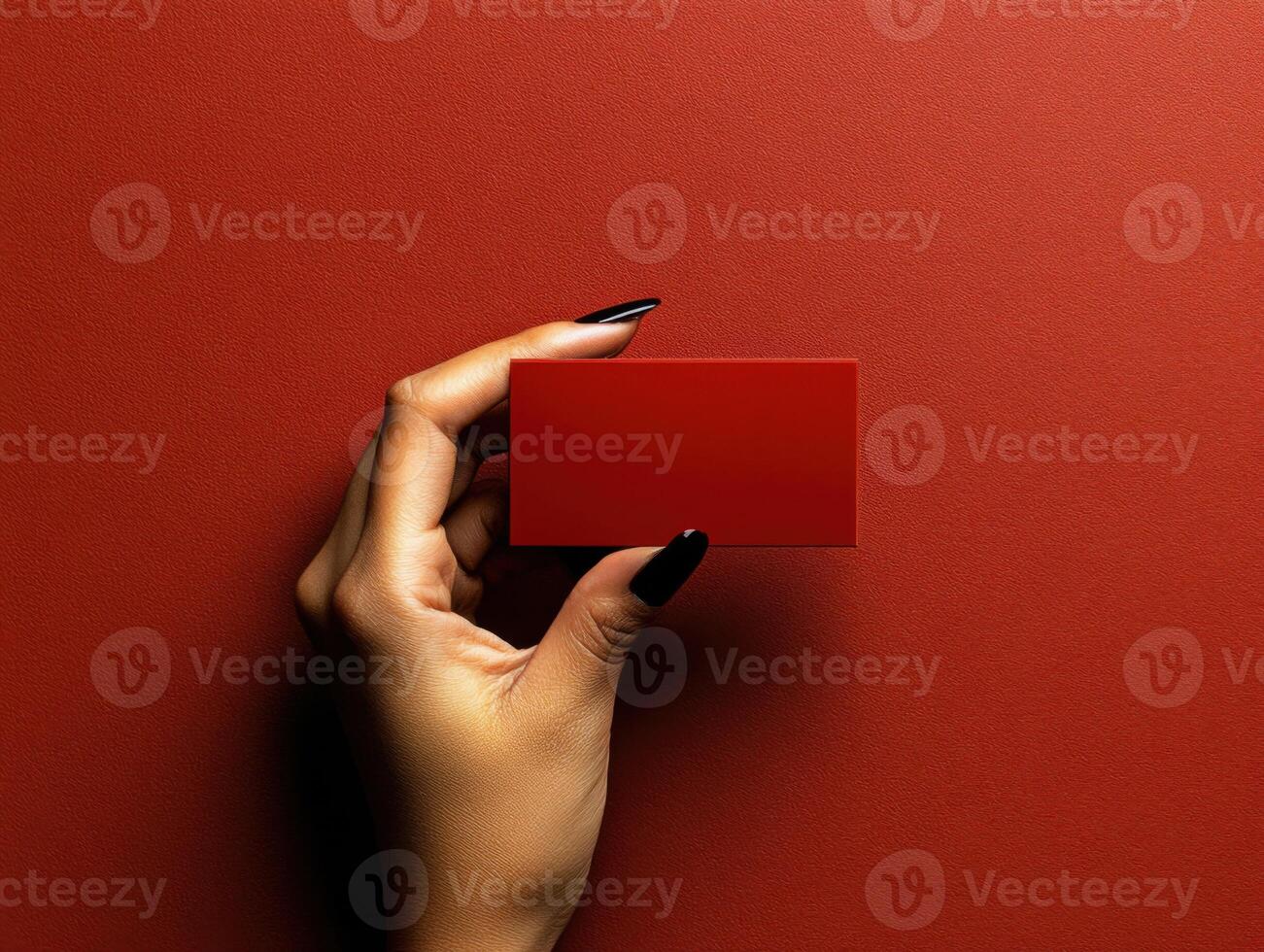 Elegant hand holding a red rectangular card against a textured red background in a minimalist setting photo