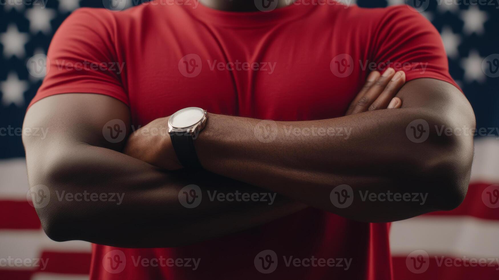Strong man with crossed arms posing in front of an American flag while wearing a red t-shirt and watch photo