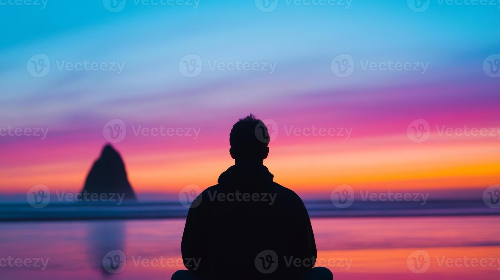 Meditation at sunset on a tranquil beach with colorful sky and distant rock formation photo