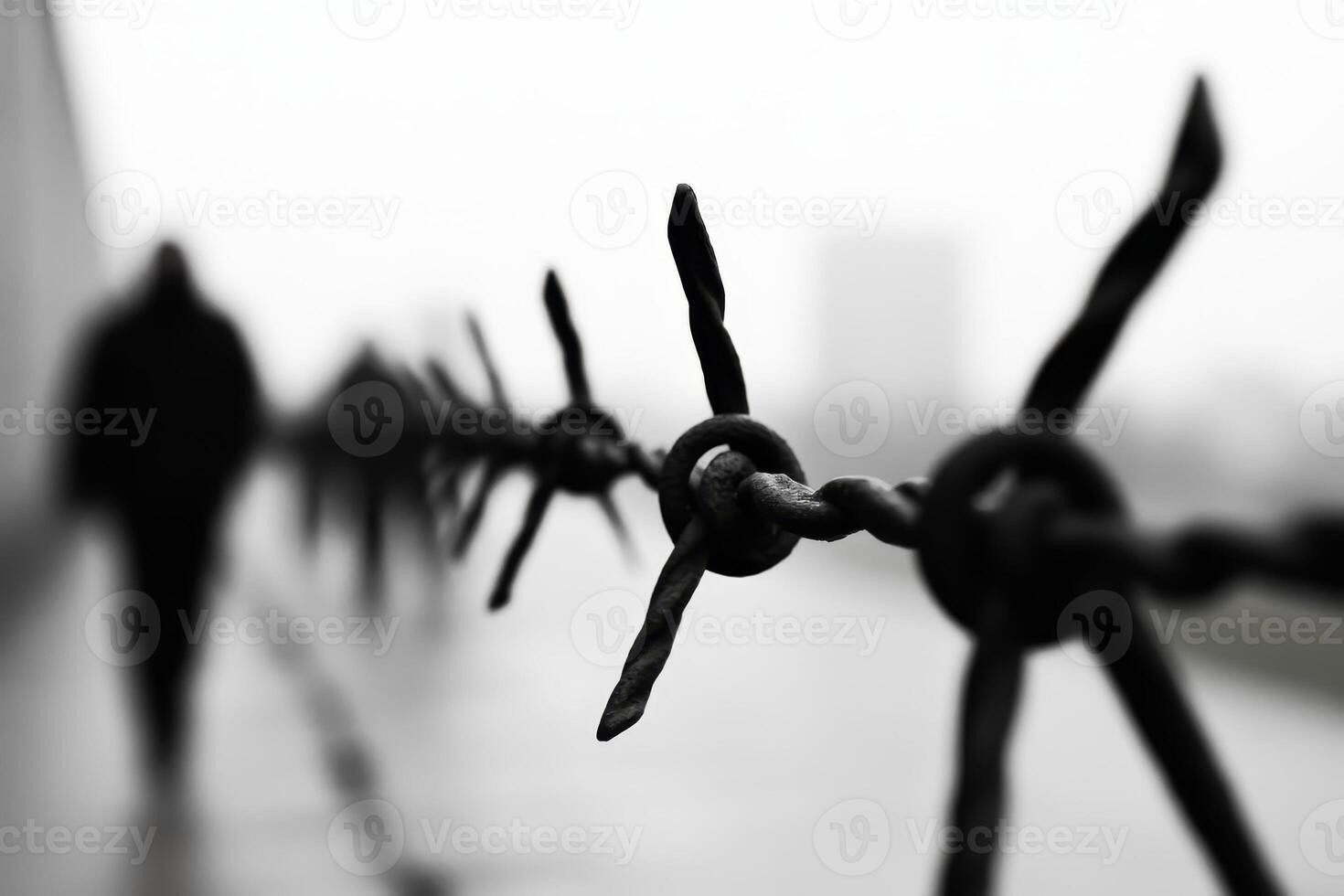 Barbed wire fence along a desolate path with shadowy figures walking in the distance during overcast weather photo