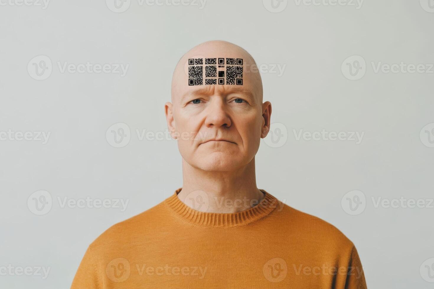 Digital slavery, digital concentration camp, social problem of the future concept. Man with QR codes on forehead poses in a neutral setting while wearing an orange sweater photo
