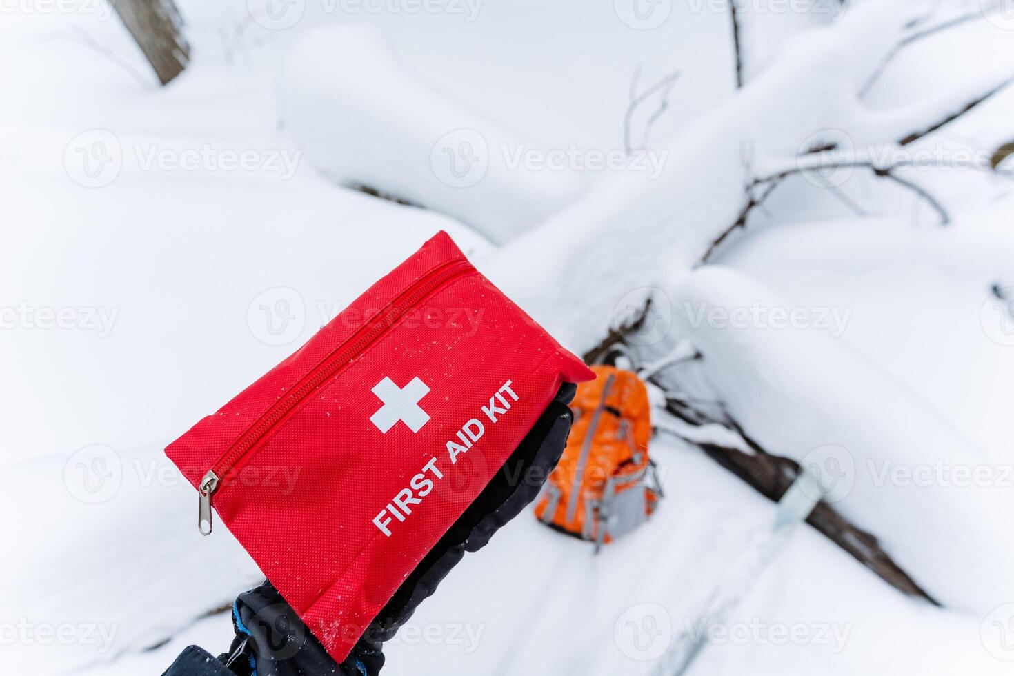 A bright red first aid kit is laying on the cold snow, standing out against the white backdrop of winters chill. It could be crucial in emergencies that arise in such conditions photo