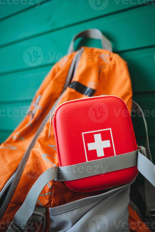 A bright red first aid kit is prominently sticking out of a large backpack, drawing attention to itself in case of any emergencies that might arise while one is out and about photo